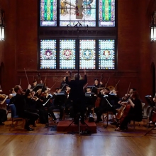 Kenneth Slowik leads the Smithsonian Academy Orchestra in a large room with stained glass windows and wood floors